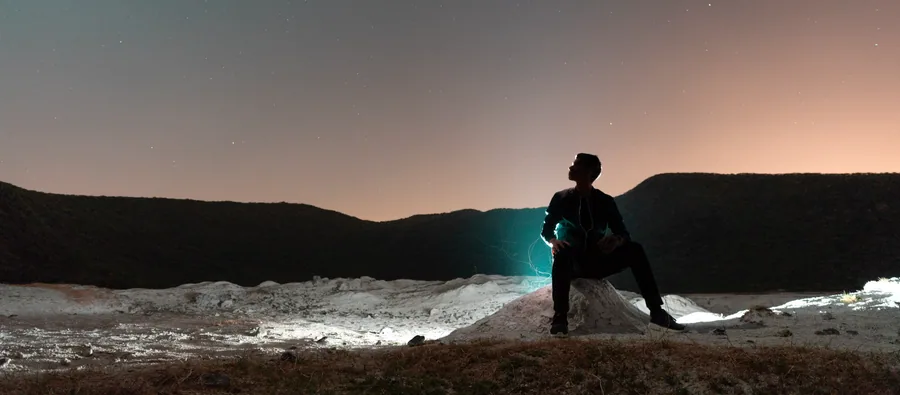 An explorer seated on a rock at dusk — the human, small inside a living system.