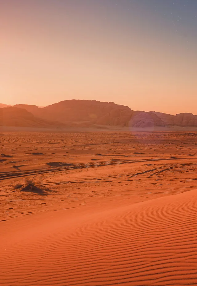 A figure seated in the desert at dusk.